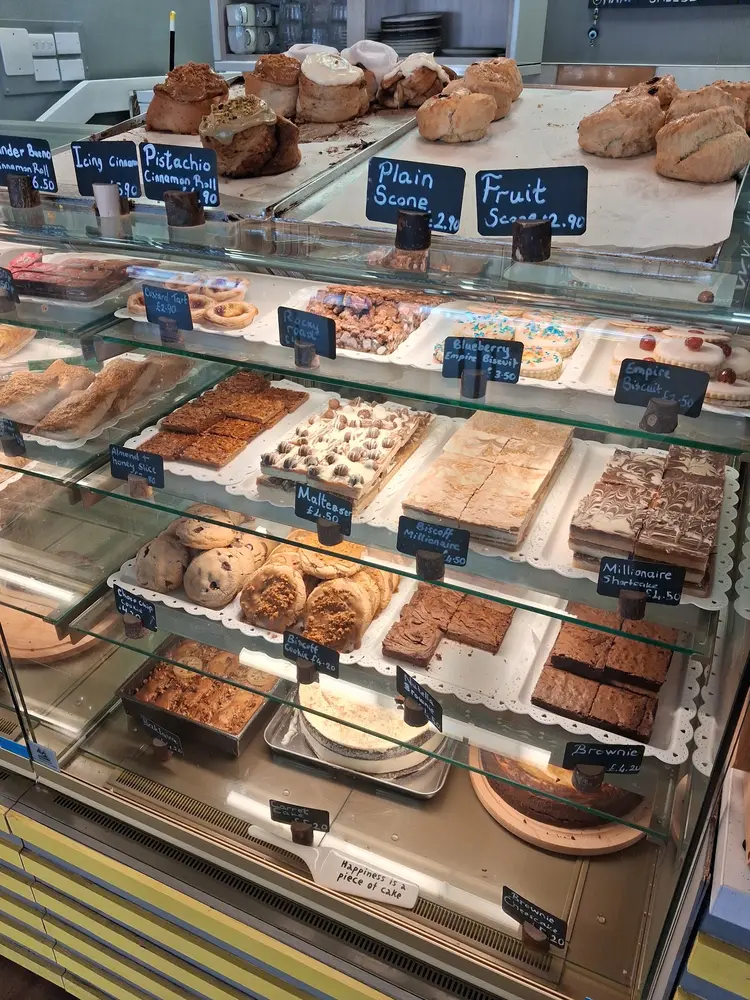 Glass display counter filled with cinnamon rolls, scones, traybakes and cookies with handwritten chalkboard price tags
