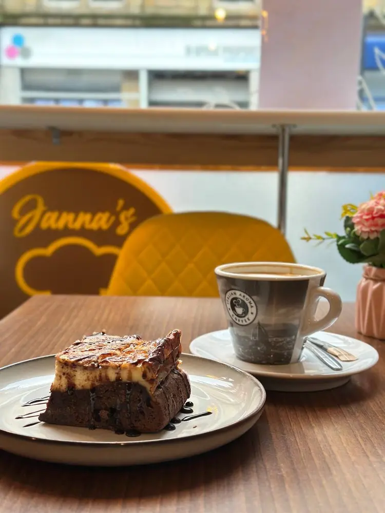 Slice of chocolate cheesecake and a cup of Italian Aroma coffee on a table, Janna's logo on the wall behind