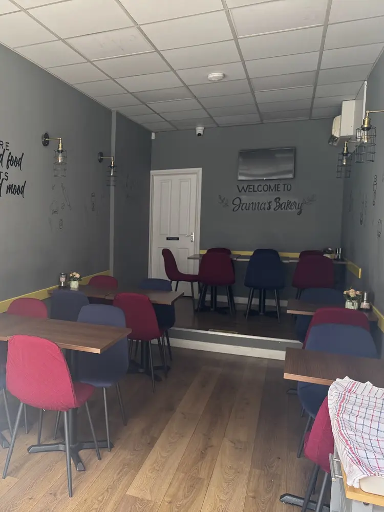 Bright seating room with grey walls, red and navy chairs, a woven Turkish rug and a Welcome to Janna's Bakery wall sign